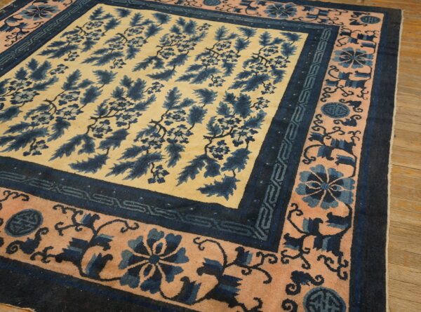 Navy blue and cream rug with foliage motif and blush borders displayed on light wood planks.