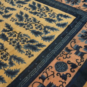 Yellow rug with dense blue foliage pattern and a wide peach and indigo border on hardwood.