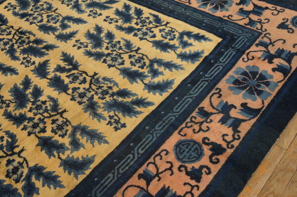 Yellow rug with dense blue foliage pattern and a wide peach and indigo border on hardwood.