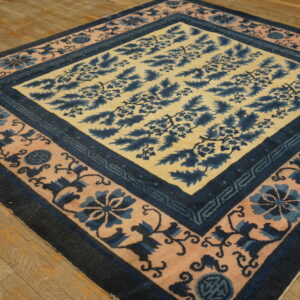 A blue and tan floral pattern rug with pink and navy borders rests diagonally on a rustic wood floor.