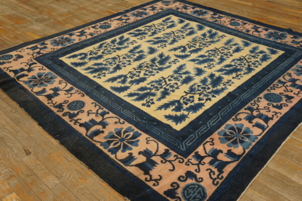 A blue and tan floral pattern rug with pink and navy borders rests diagonally on a rustic wood floor.