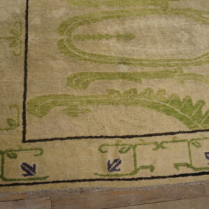 Textured beige rug with olive green vine motifs and dark indigo accents on light brown wood planks.