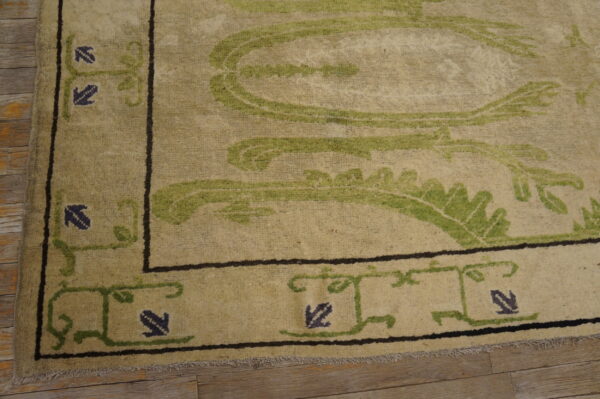Textured beige rug with olive green vine motifs and dark indigo accents on light brown wood planks.
