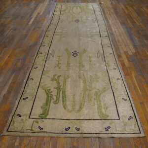 Beige runner rug with bold green abstract patterns and dark geometric borders on distressed wood planks.