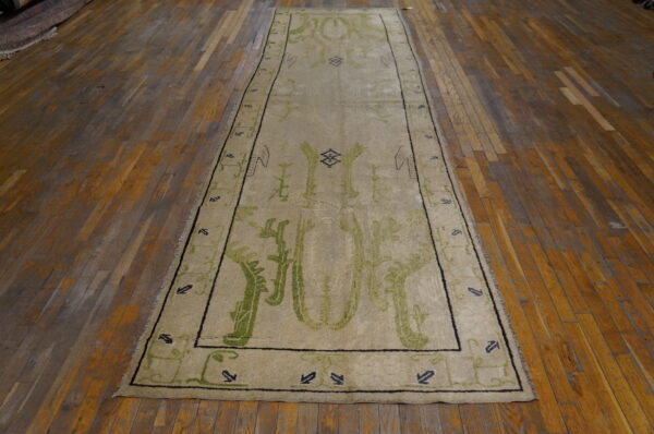Beige runner rug with bold green abstract patterns and dark geometric borders on distressed wood planks.