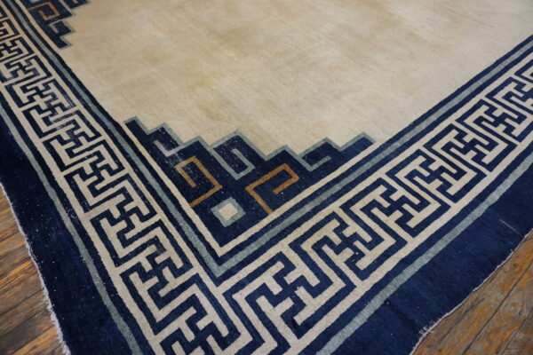 Light beige rug featuring a wide navy blue and cream fretwork border rests on distressed wood flooring.