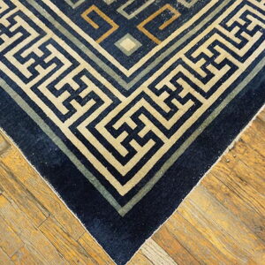 Geometric navy blue rug with beige and green fretwork border on distressed hardwood flooring.