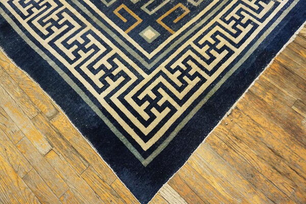 Geometric navy blue rug with beige and green fretwork border on distressed hardwood flooring.