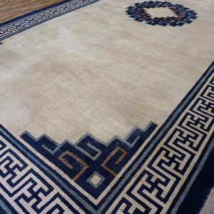 Light beige rug featuring a dark blue geometric border and center roundel on rustic wood planks.