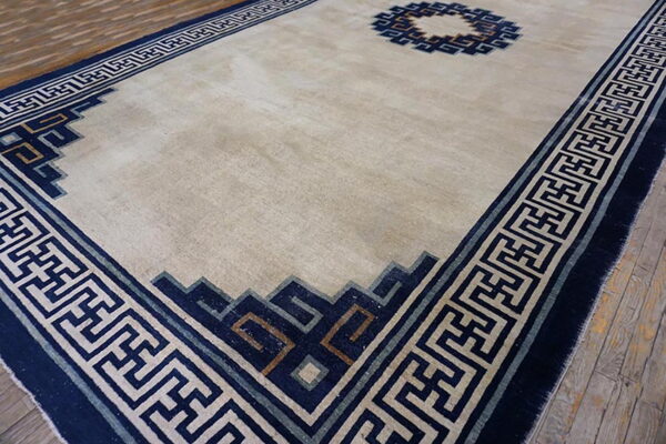 Light beige rug featuring a dark blue geometric border and center roundel on rustic wood planks.
