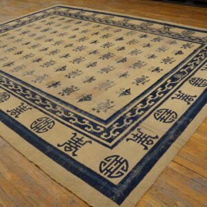 Low-pile beige rug with dark blue floral and symbolic borders rests on a distressed wooden floor.