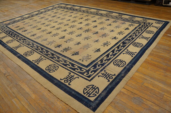 Low-pile beige rug with dark blue floral and symbolic borders rests on a distressed wooden floor.