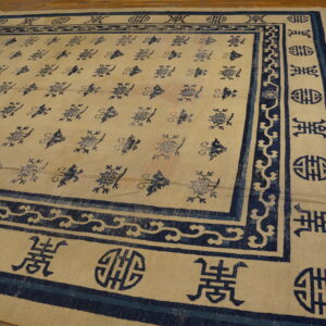 Beige rug featuring repeating navy floral motifs and wide borders with symbolic blue designs on hardwood.