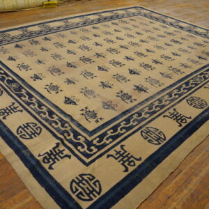 Beige rug with all-over navy symbols and wide borders lies on worn plank hardwood flooring.