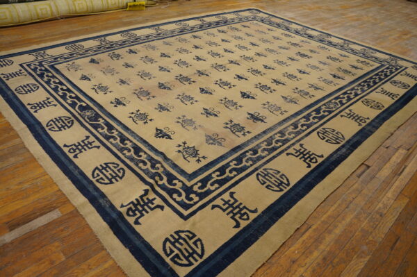 Beige rug with all-over navy symbols and wide borders lies on worn plank hardwood flooring.