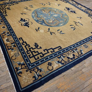 Low-pile beige rug with complex blue geometric and dragon patterns rests on distressed wooden floors.