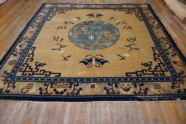 Tan and blue rug featuring two dragons in a central medallion, displayed on distressed wooden floorboards.