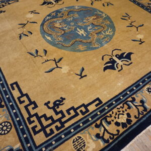 Low pile tan rug with a blue dragon medallion and dark blue geometric borders rests on wood floors.