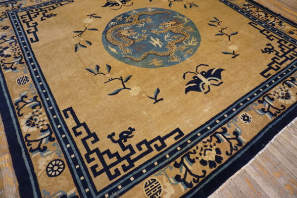 Low pile tan rug with a blue dragon medallion and dark blue geometric borders rests on wood floors.