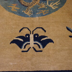 A tan area rug with a navy blue butterfly pattern and scattered floral sprigs around a blue dragon medallion.