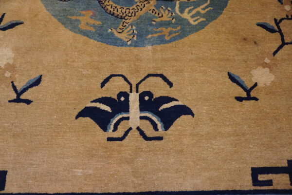 A tan area rug with a navy blue butterfly pattern and scattered floral sprigs around a blue dragon medallion.