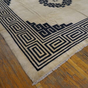 Beige rug featuring a bold black Greek Key border and geometric motifs on distressed hardwood floors.