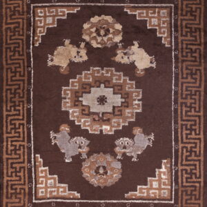 Dark brown rug featuring a geometric key pattern border, central medallion, and stylized animal figures in tan and gray.