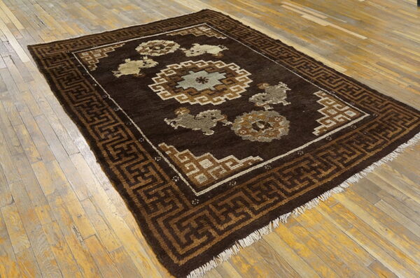 Dark brown low-pile rug with tan and sage geometric patterns rests on worn, light wood plank flooring.
