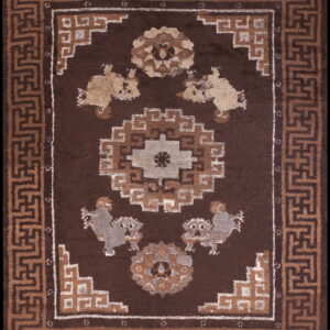 Dark brown rug featuring a central geometric medallion and four stylized figures framed by a tan fret border.