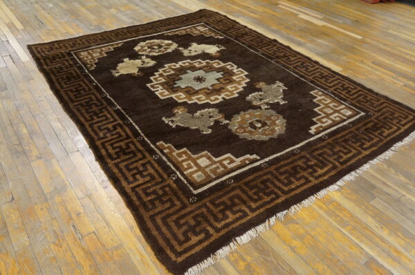 Dark brown rug featuring geometric and central medallion patterns in tan and light gray on rustic wood floors.