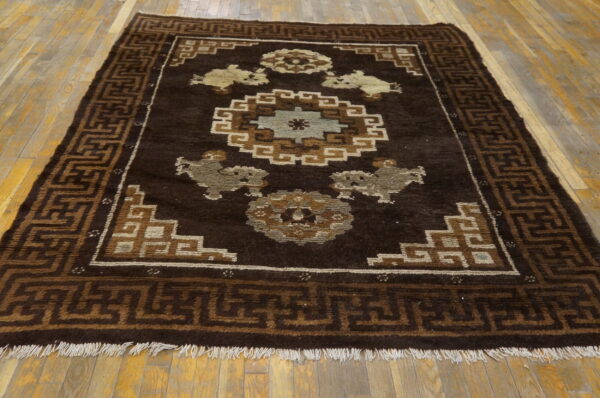 Dark brown geometric rug with tan, cream, and blue stylized motifs on natural wood flooring.