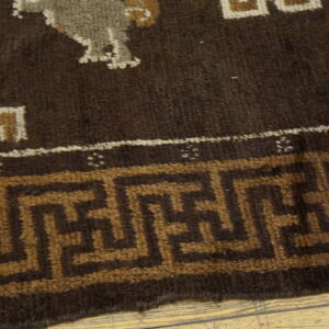 Close-up of a dark brown rug featuring geometric patterns and a Greek Key border on light wood.