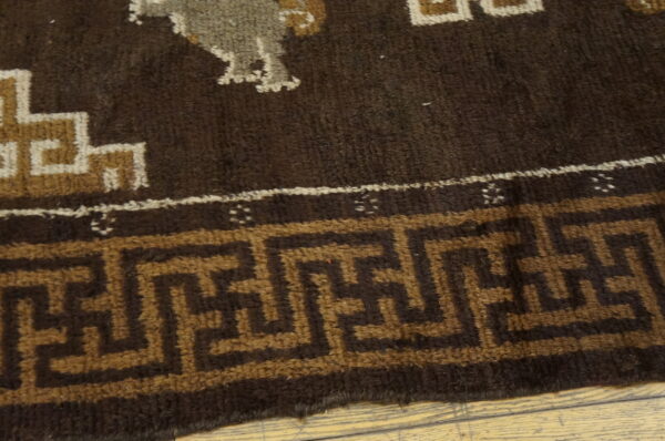 Close-up of a dark brown rug featuring geometric patterns and a greek key border on light wood.