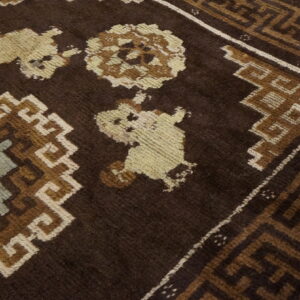 Angled view of a dark brown rug featuring light tan and blue geometric medallions on wood flooring.
