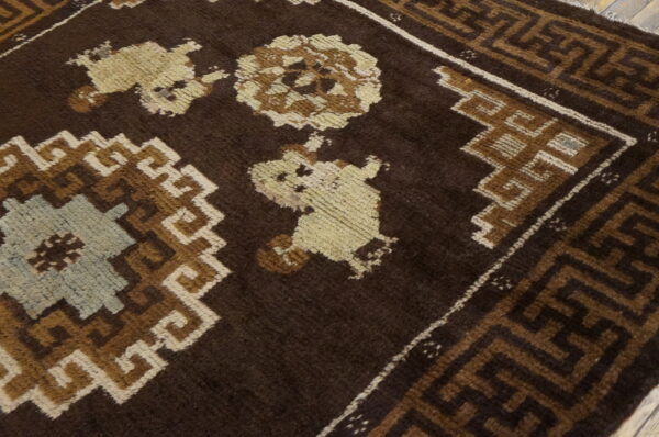 Angled view of a dark brown rug featuring light tan and blue geometric medallions on wood flooring.