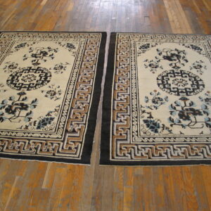 Pair of traditional rugs with cream fields, complex key borders, and dark floral patterns on wood planks.