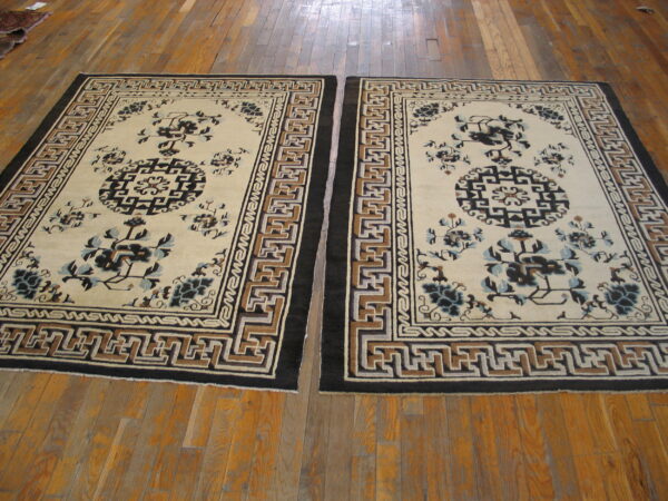 Pair of traditional rugs with cream fields, complex key borders, and dark floral patterns on wood planks.