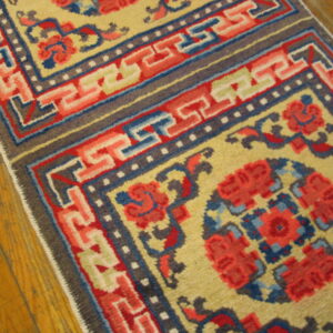 Low-pile yellow rug runner with red, blue, and gray geometric borders rests on wood flooring.