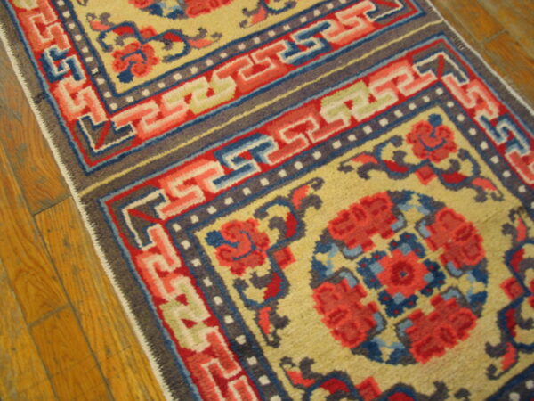 Low-pile yellow rug runner with red, blue, and gray geometric borders rests on wood flooring.