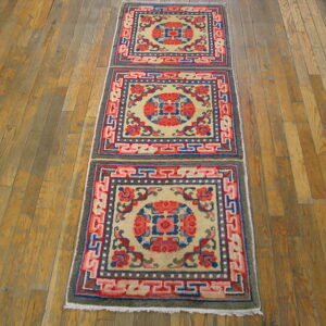 Long, low pile runner rug featuring cream, red, and blue repeating geometric medallions on a hardwood floor.
