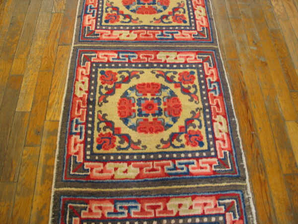 Low-pile runner with bold red, blue, and yellow squares and key fret borders on wood planks.