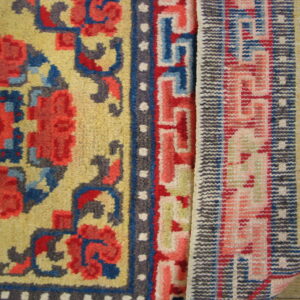 Detail of a yellow high-pile rug and a pink flatweave rug displayed on wood planks.