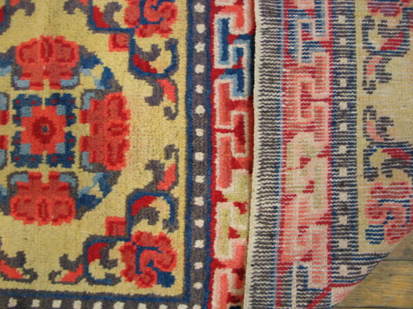 Detail of a yellow high-pile rug and a pink flatweave rug displayed on wood planks.