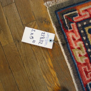 Multi-colored geometric rug corner with fringe and white price tag resting on distressed wood planks.