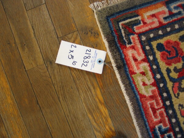 Multi-colored geometric rug corner with fringe and white price tag resting on distressed wood planks.