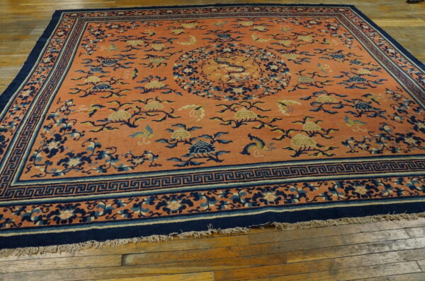 Orange field rug with complex navy and cream floral patterns and an ornate greek key border on wood floor.