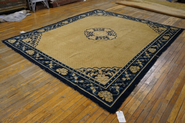 Golden tan rug with a navy blue border featuring detailed floral motifs on hardwood floors.