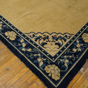 Close-up of a golden and navy rug corner featuring scrolling floral motifs on distressed wood flooring.