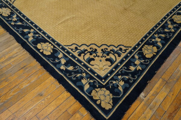Close-up of a golden and navy rug corner featuring scrolling floral motifs on distressed wood flooring.