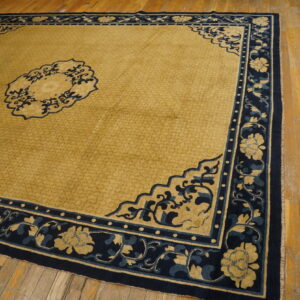Low-pile gold rug featuring a navy blue floral border and medallion, displayed on aged wooden flooring.